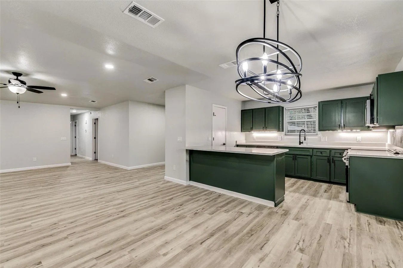 Kitchen and living area joined into one room after a load-bearing wall was removed, with deep green cabinetry and light wide-plank flooring in a completed Plano, Texas whole-home remodel.
