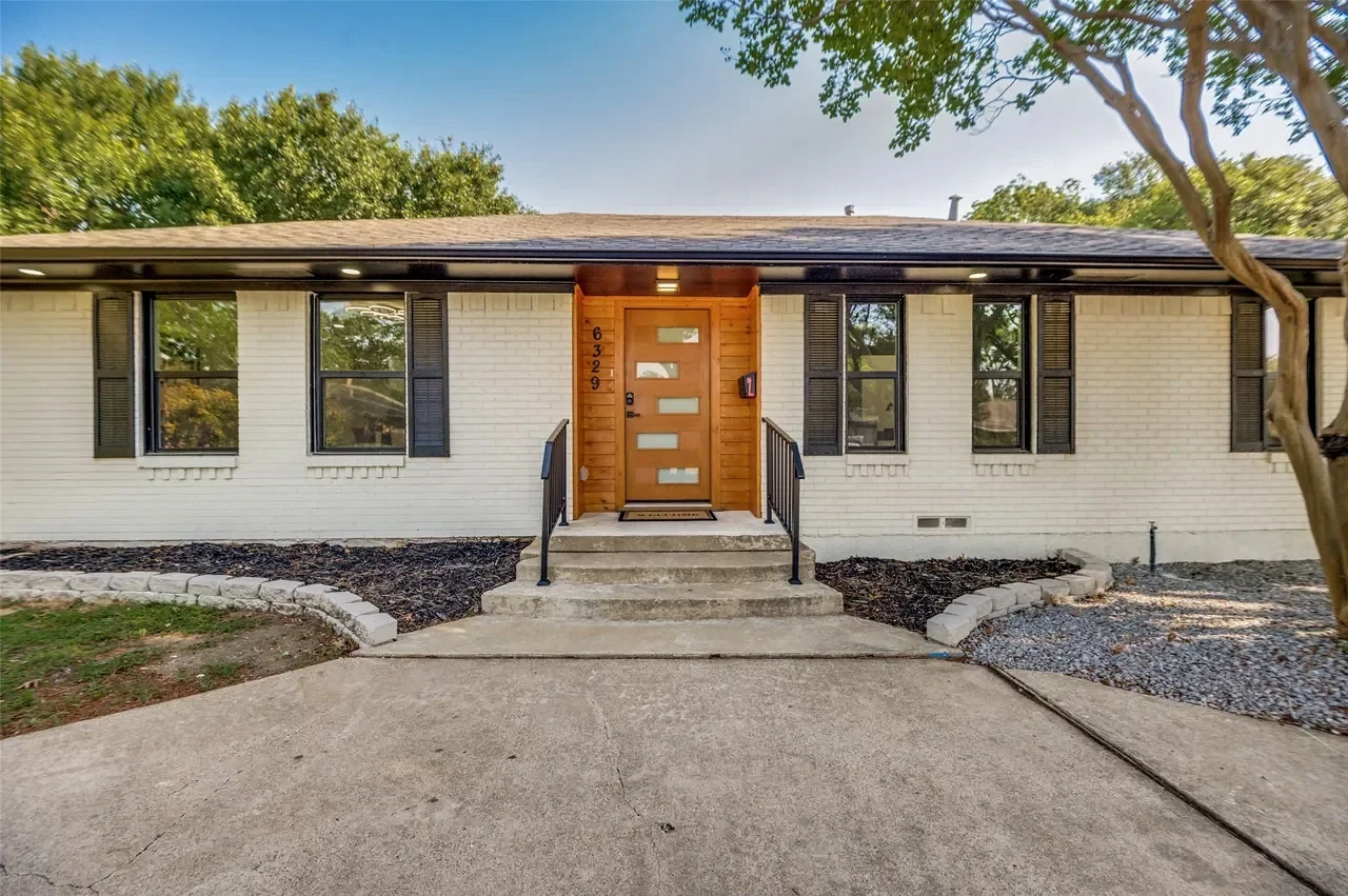 White brick single-storey residence with a wood front door and mature tree, photographed after completion in Lower Greenville, Dallas, Texas.