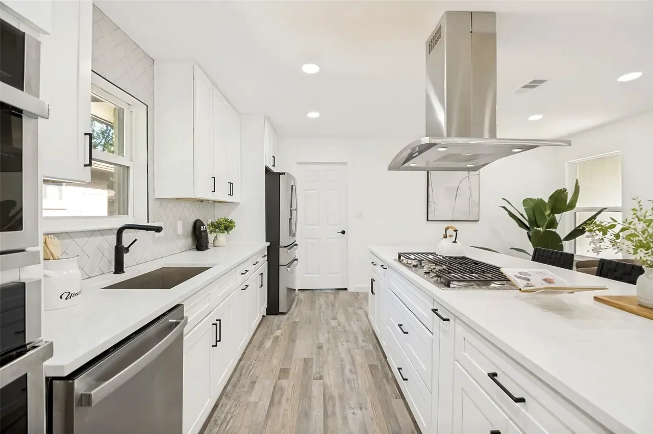 White kitchen with a stainless range, marble-look counters and a black tap in a completed Lower Greenville, Dallas whole-home remodel.