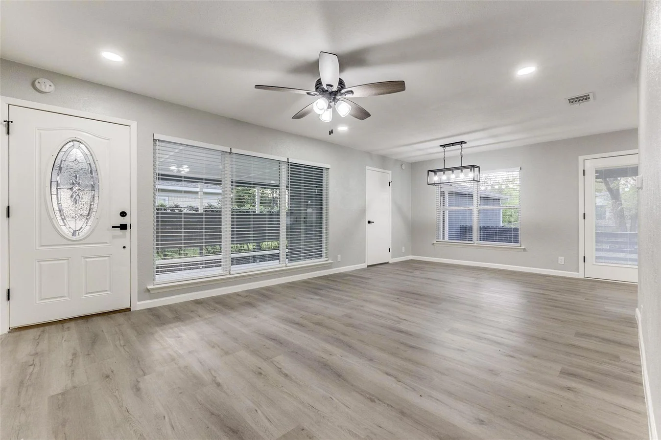 Open living room with gray wood-look flooring, broad windows, recessed lighting, and direct access to the kitchen in Dallas, Texas.