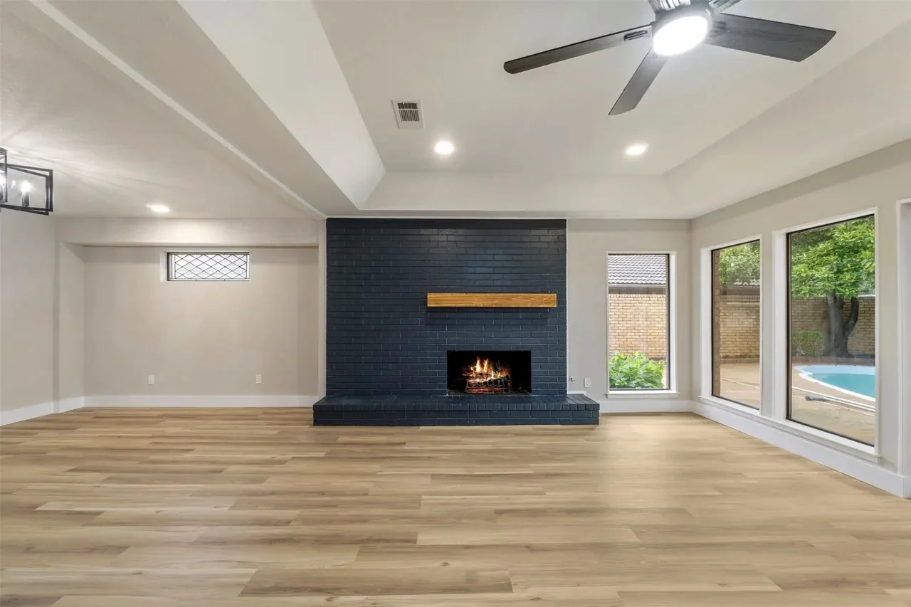 Open living area after structural wall removal with a black fireplace, wide-plank flooring, recessed lighting, and pool views in Fort Worth, Texas.