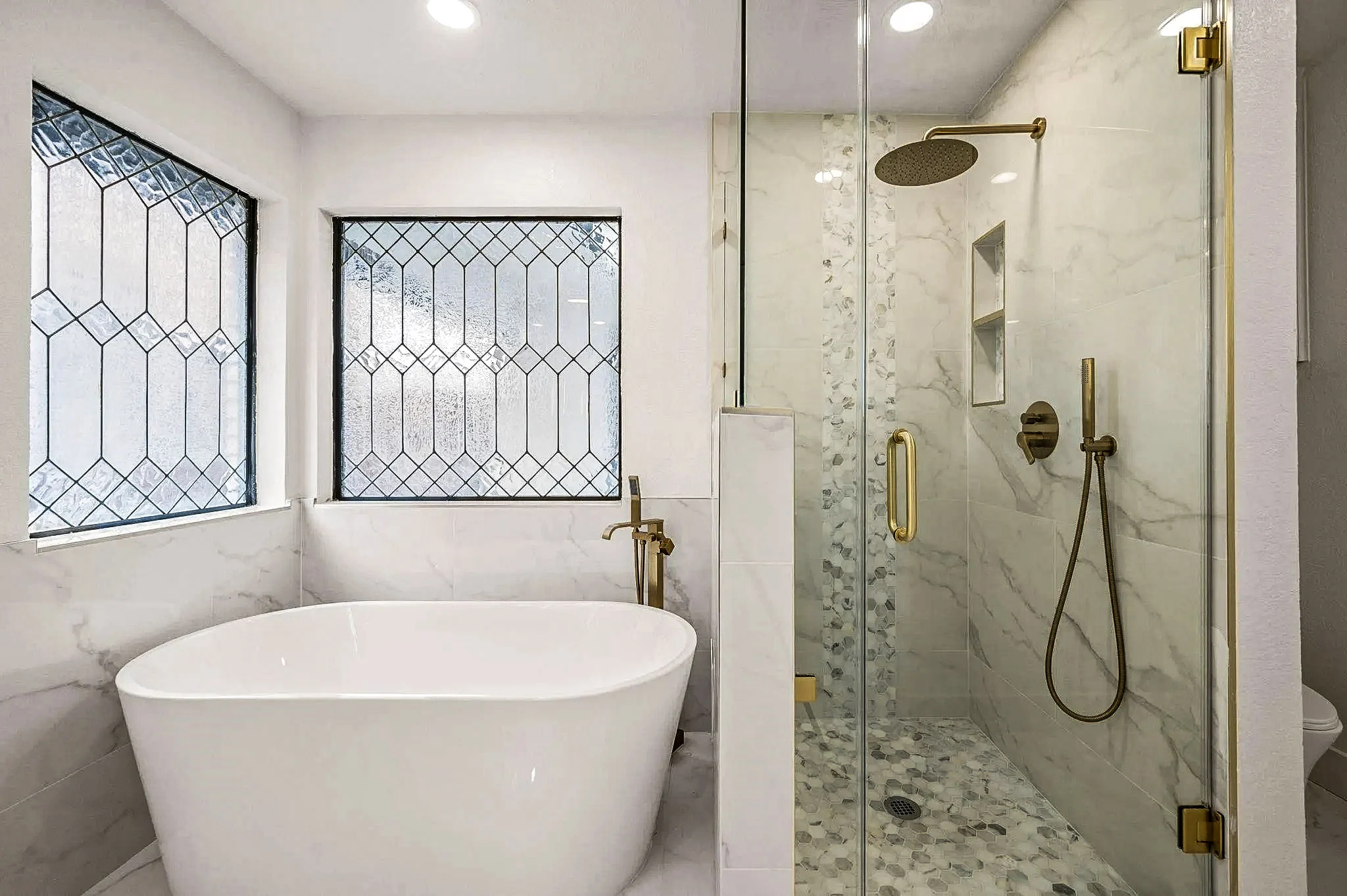 Primary bathroom wet room with a freestanding tub, marble-look shower, brass fixtures, and decorative black-framed windows in Grapevine, Texas.