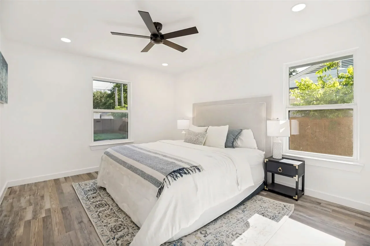 Secondary bedroom with white walls, wood-look flooring, black ceiling fan, corner windows, and staged furnishings in Lower Greenville, Dallas, Texas.