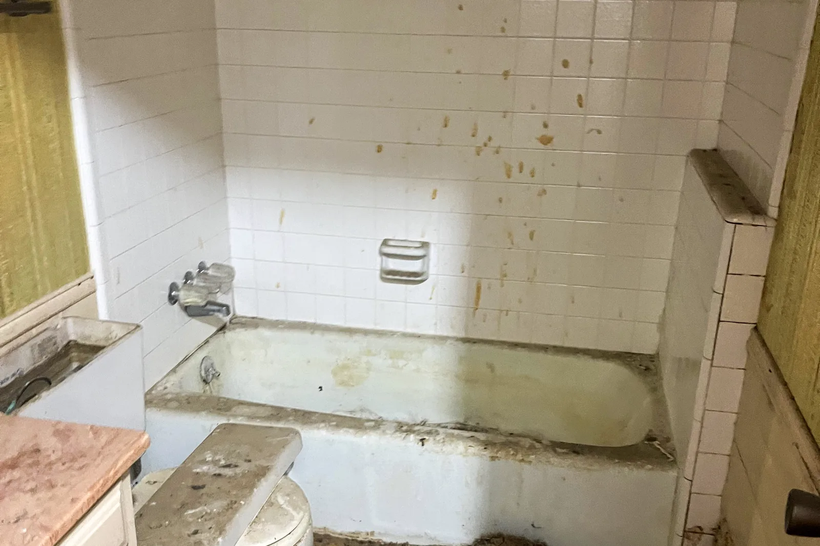 Plano guest bathroom before renovation, with the original alcove tub, white square tile surround, dated vanity, and a stripped floor.