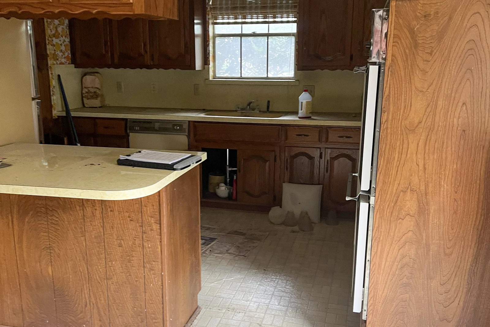 The Plano kitchen before renovation, with original wood cabinetry, laminate counters and a damaged tile floor.
