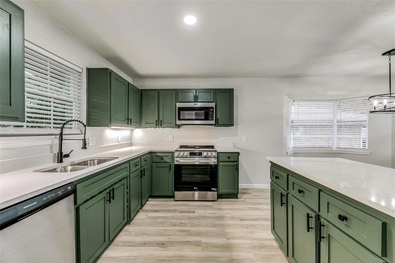 Deep green shaker kitchen with a large white island, stainless steel appliances, black fixtures, and light wood-look flooring in Plano, Texas.