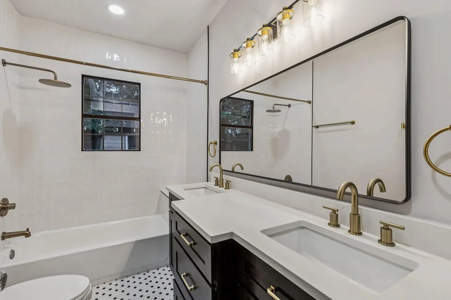 Dallas double-vanity bathroom with white cabinetry, brass fixtures, black-framed mirror, and marble-look counter.