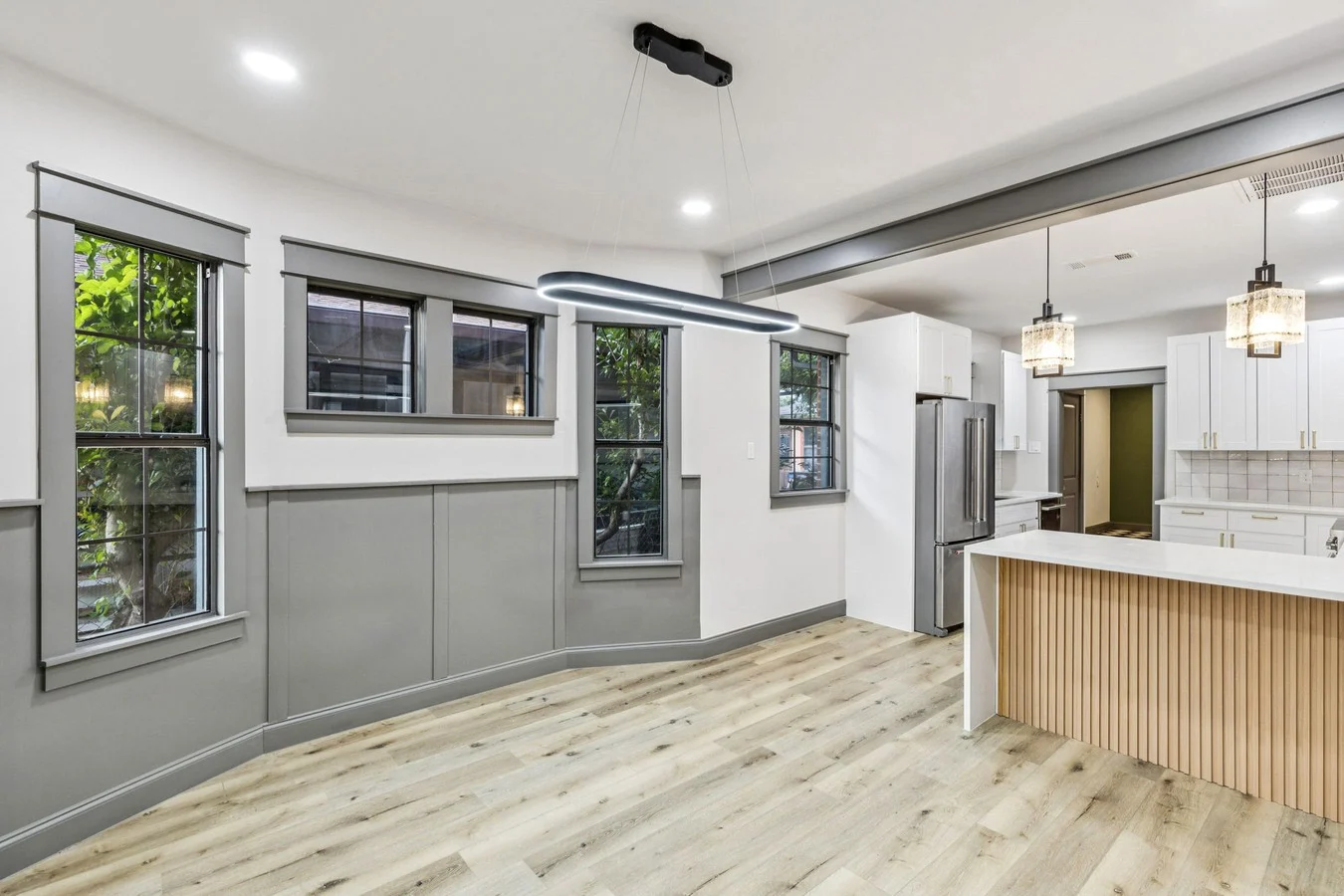Kitchen and living connection with a fluted wood island, gray wall paneling, black-framed windows, and light wood-look flooring in Bishop Arts, Dallas, Texas.