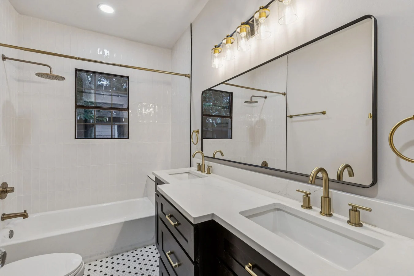 Guest bathroom with a tub and shower, white vanity, broad mirror, and brushed brass fixtures in Bishop Arts, Dallas, Texas.