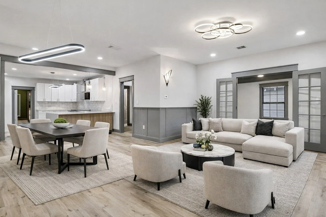 Open living and dining area connected to the kitchen with light flooring, gray wall paneling, and contemporary lighting in Bishop Arts, Dallas, Texas.