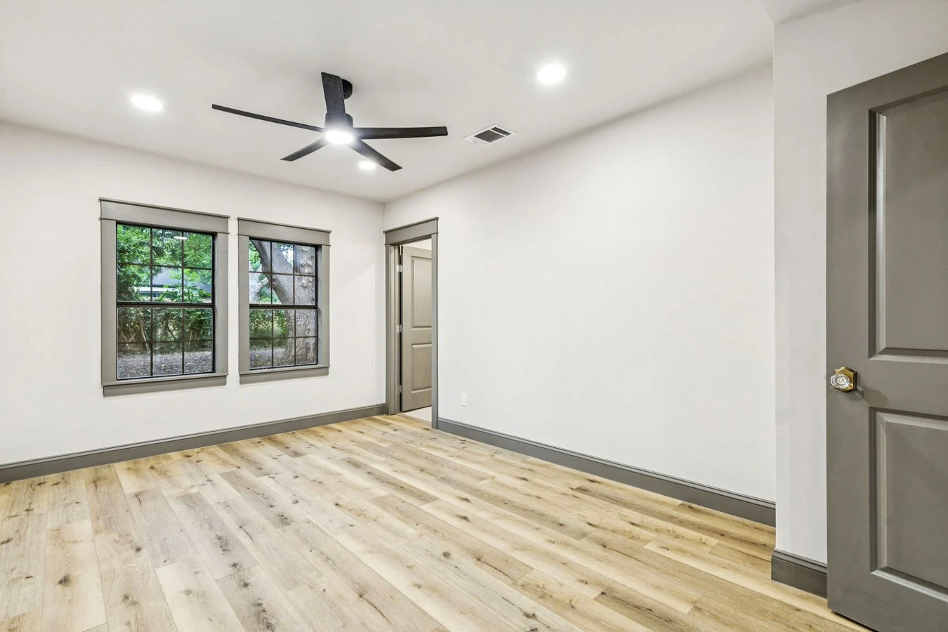 New primary bedroom with black-framed windows, light wood-look flooring, white walls, and charcoal trim in Bishop Arts, Dallas, Texas.