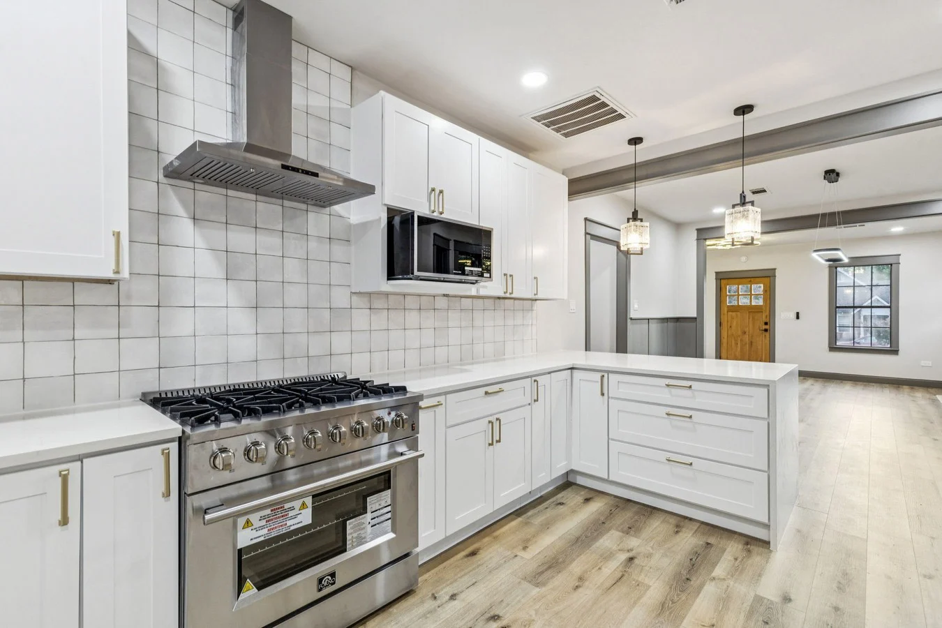 White U-shaped kitchen with a professional-style range, subway tile backsplash, brass hardware, and pendant lighting in Bishop Arts, Dallas, Texas.
