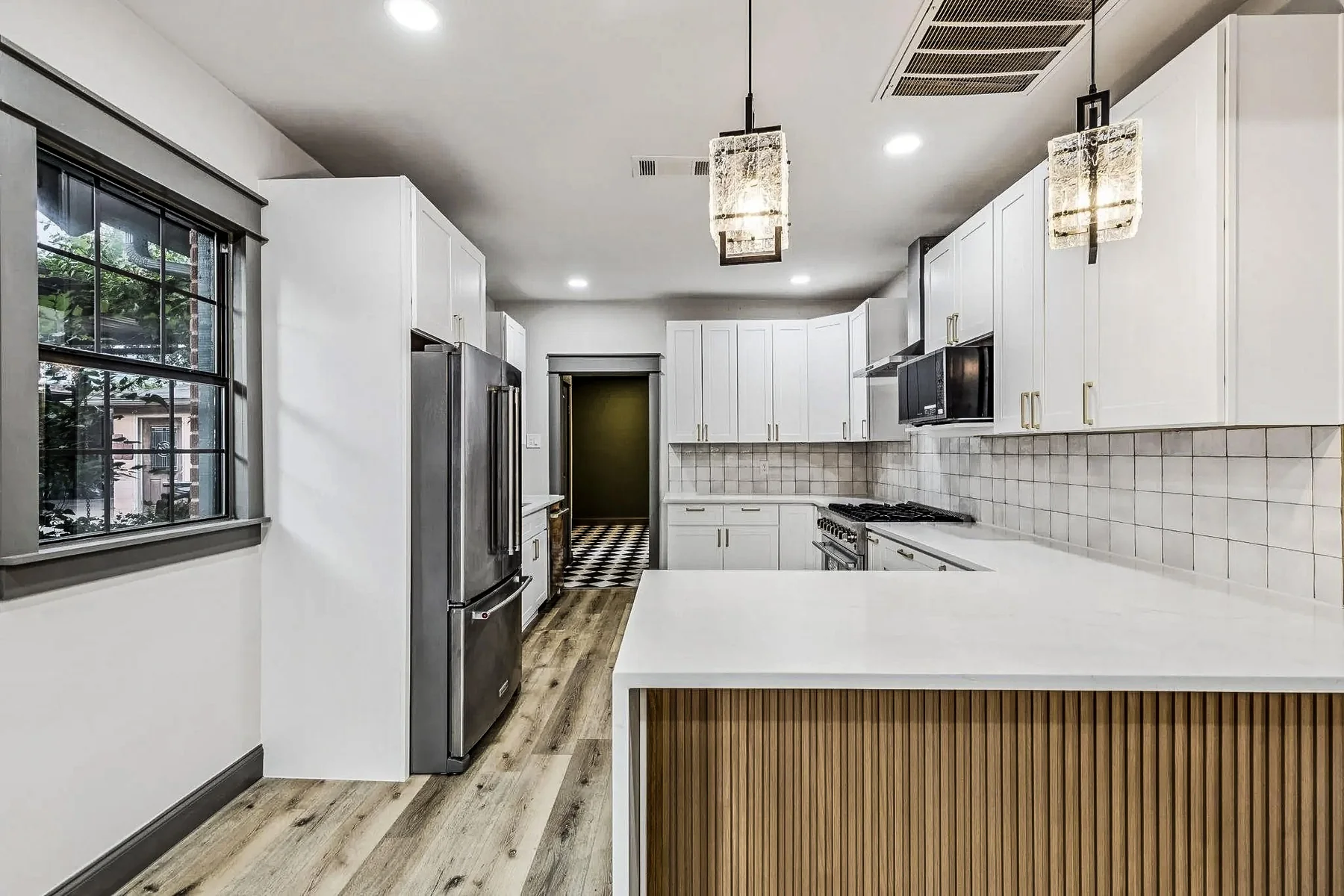 White kitchen with waterfall island, black appliances, pendant lights, and a fluted wood island panel in Bishop Arts, Dallas.