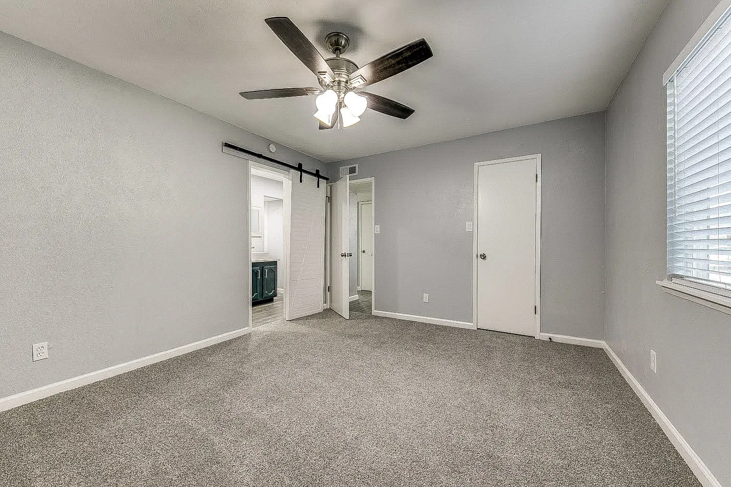 Dallas bedroom with new gray carpet, light walls, ceiling fan, and adjoining doorway.