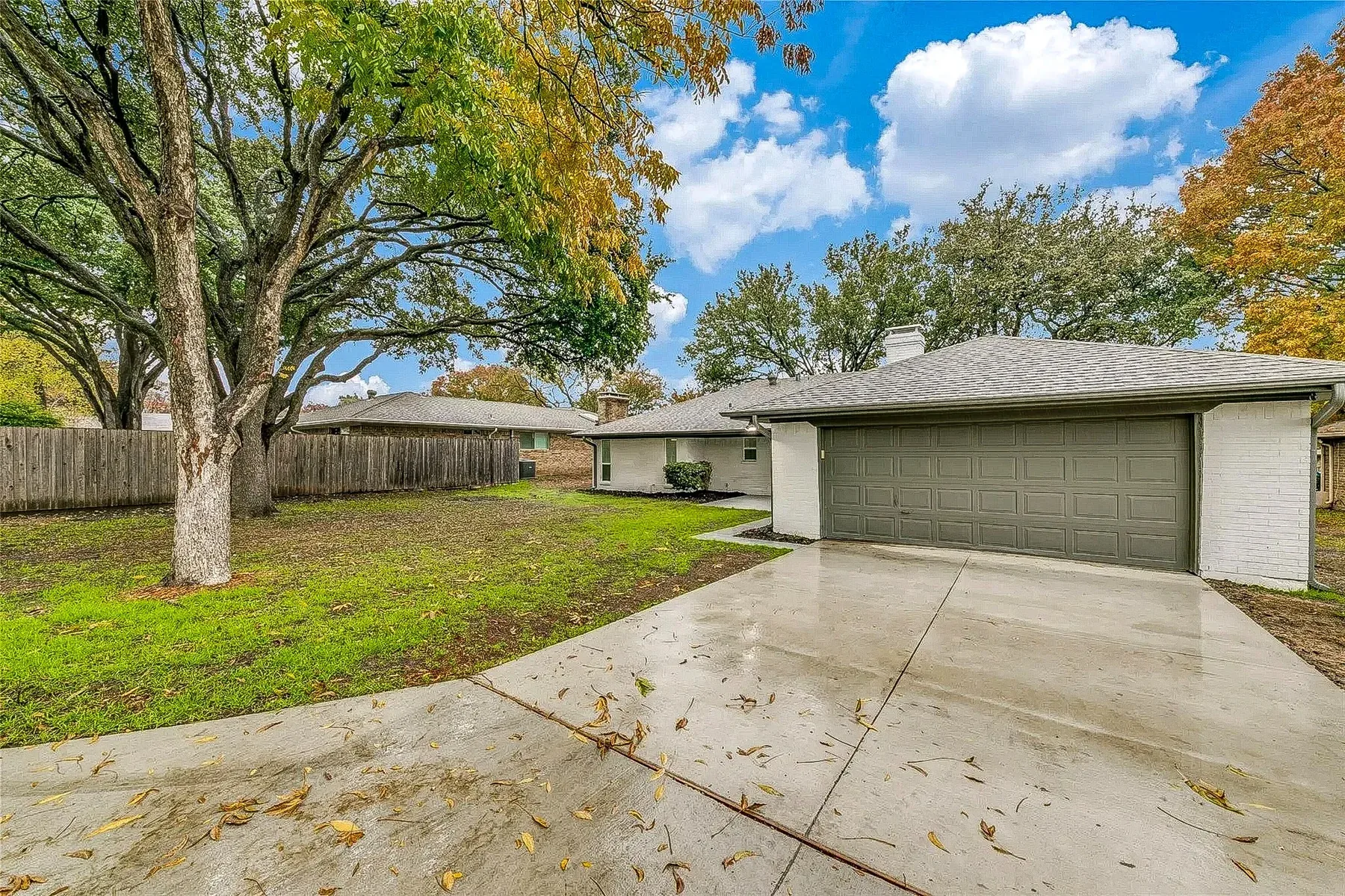 Plano home with replacement concrete driveway, two-car garage, mature tree, and landscaped front yard.