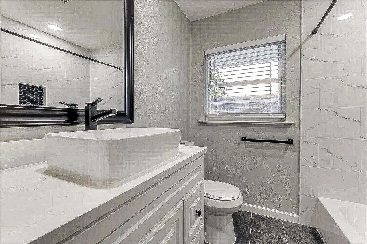 Compact bathroom with white vanity, vessel sink, black fixtures, and marble-look tub surround in Dallas.