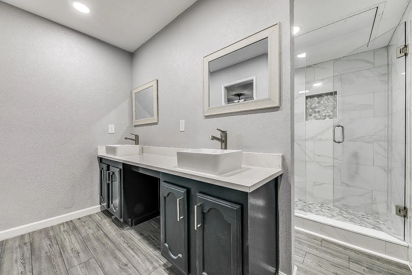 Primary bathroom with dark double vanity, vessel sinks, gray tile floor, and glass shower in Dallas.