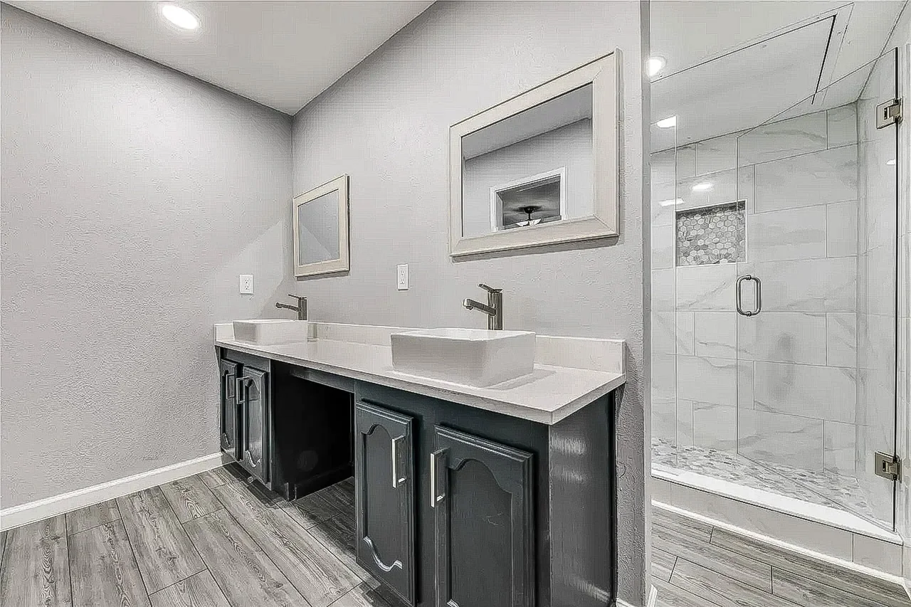 Primary bathroom with dark double vanity, vessel sinks, white counters, and frameless glass shower in Dallas.