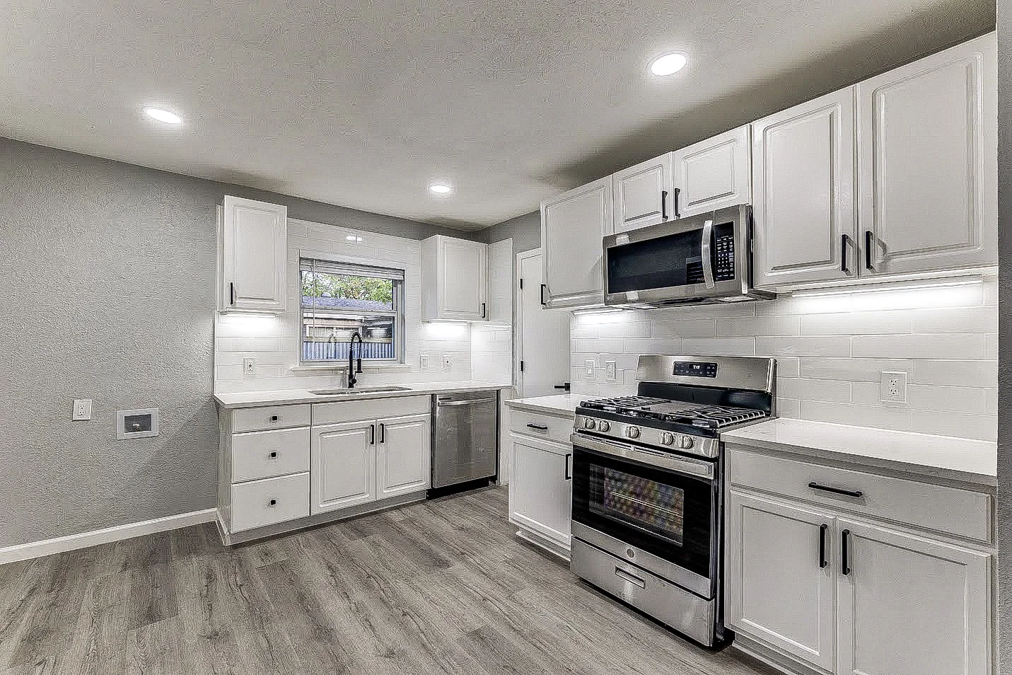 Kitchen with white shaker cabinets, gray counters, stainless steel appliances, and open living area in Dallas.