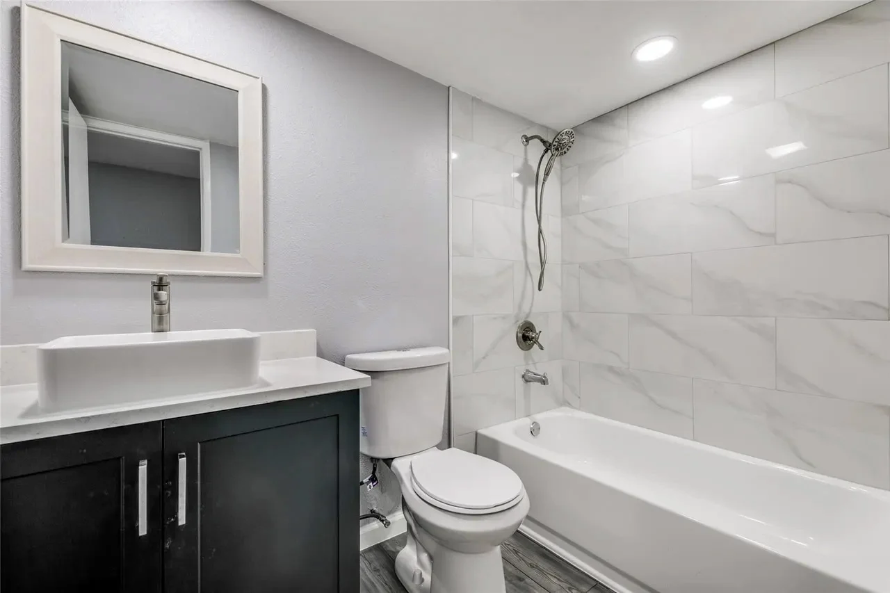 Guest bathroom with a dark vanity, white vessel sink, marble-look tub surround, chrome fixtures, and recessed lighting in Dallas, Texas.