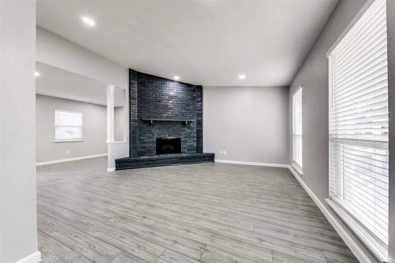Living room with new gray wood-look flooring, a black brick fireplace, recessed lighting, and broad windows in Dallas, Texas.