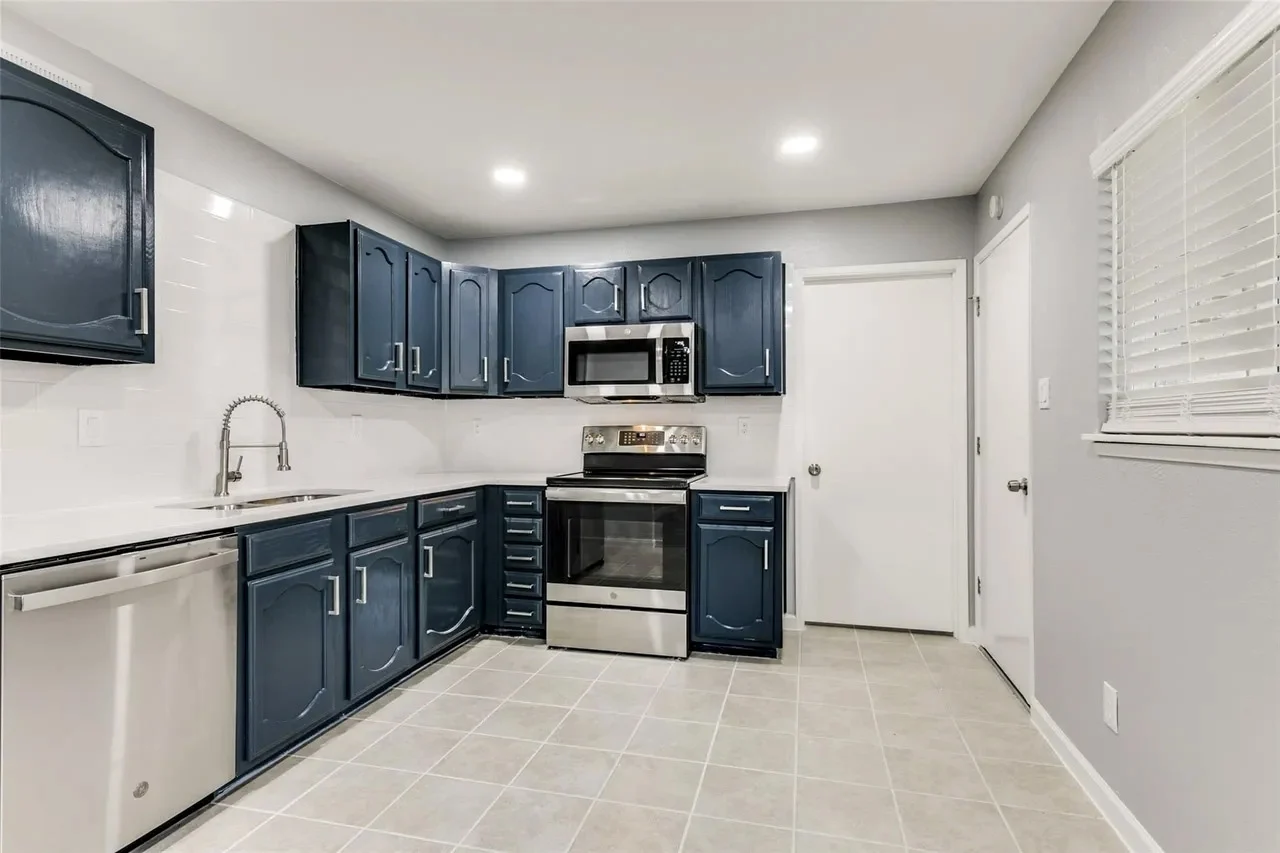 Kitchen with navy cabinetry, white counters, stainless steel appliances, neutral tile floor, and bright task lighting in Dallas, Texas.