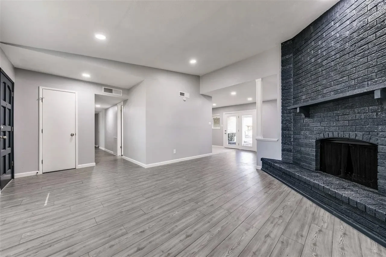 Open living area with a black brick fireplace, gray wood-look flooring, recessed lighting, and connected circulation in Dallas, Texas.
