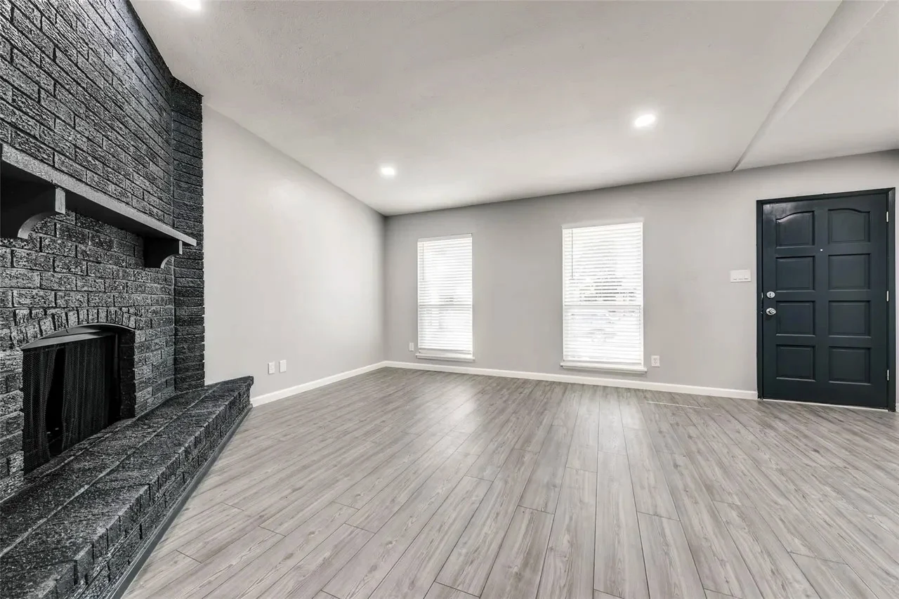 Freshly painted living room with a black brick fireplace, gray wood-look flooring, white trim, and recessed lighting in Dallas, Texas.