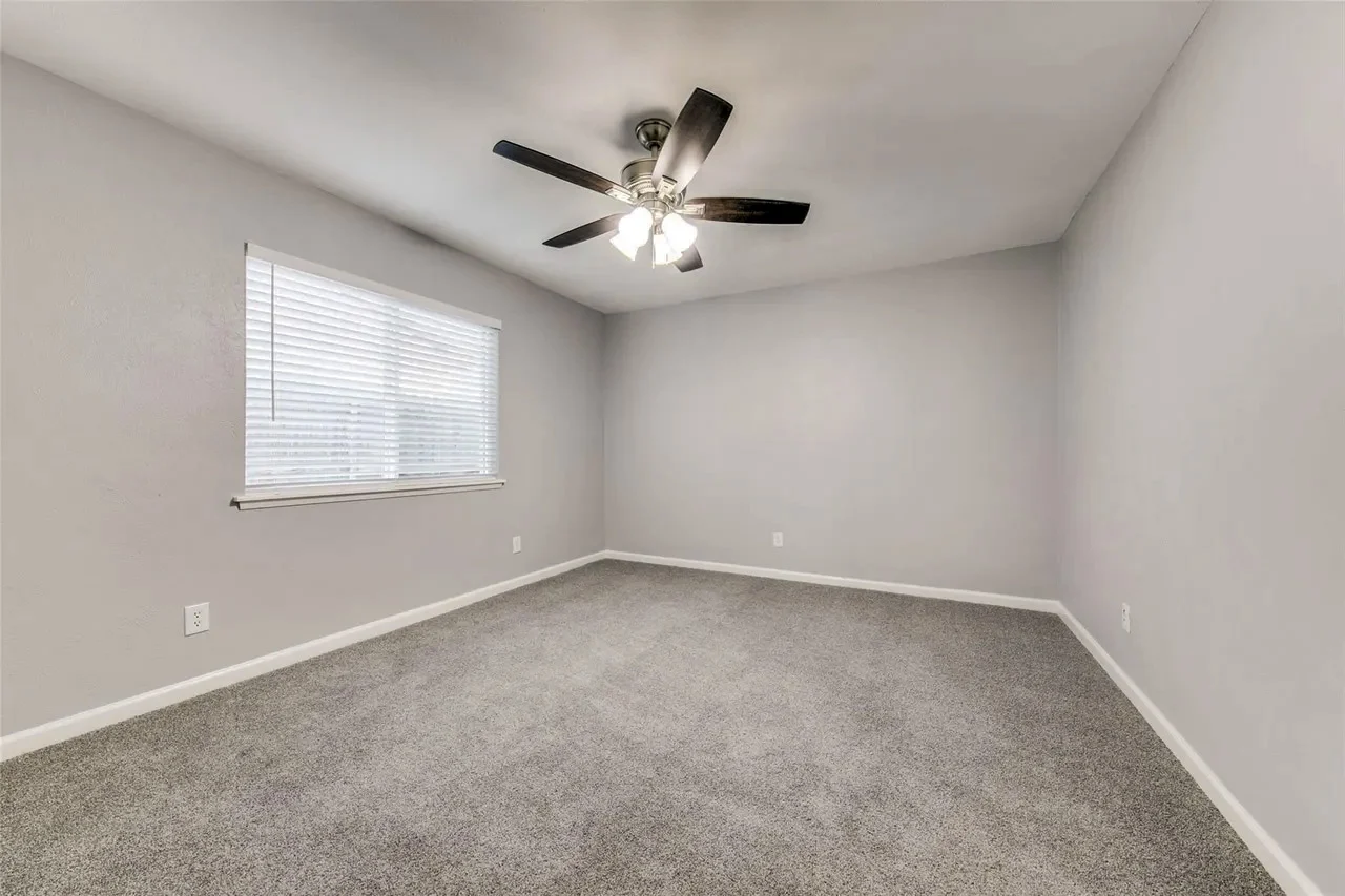 Primary bedroom with new gray carpet, light gray walls, white trim, broad window, and dark ceiling fan in Dallas, Texas.