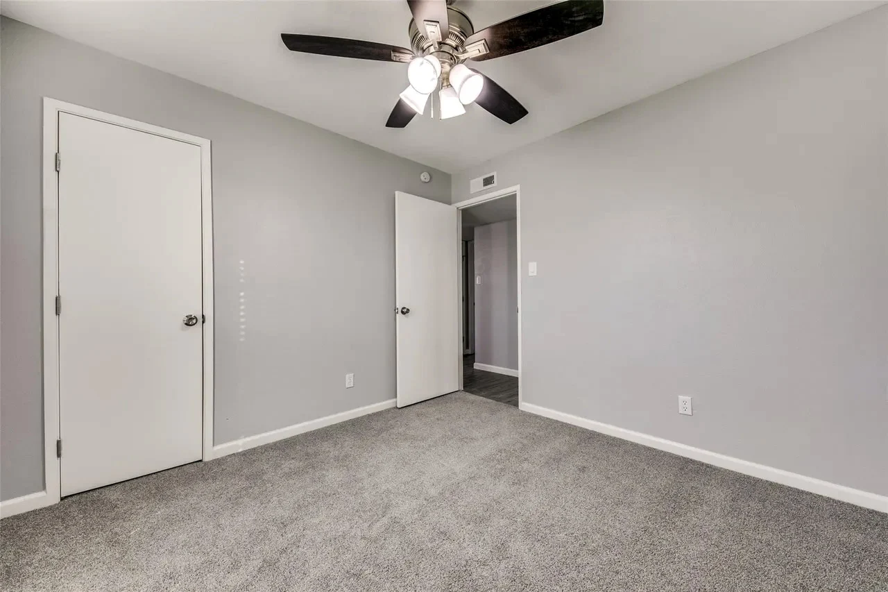 Secondary bedroom with new gray carpet, light gray walls, white trim, and a dark ceiling fan in Dallas, Texas.