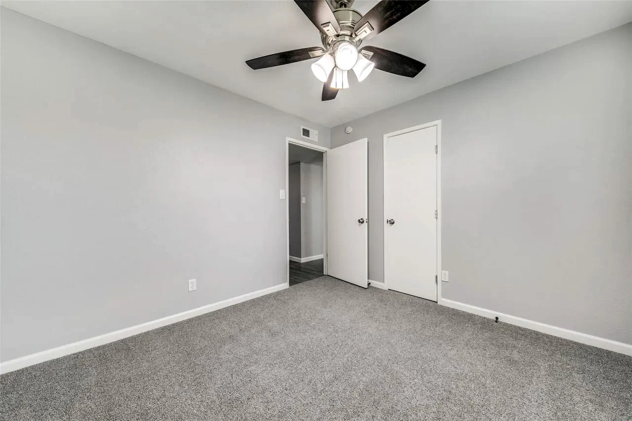 Secondary bedroom with new gray carpet, light gray walls, two closets, white trim, and a dark ceiling fan in Dallas, Texas.