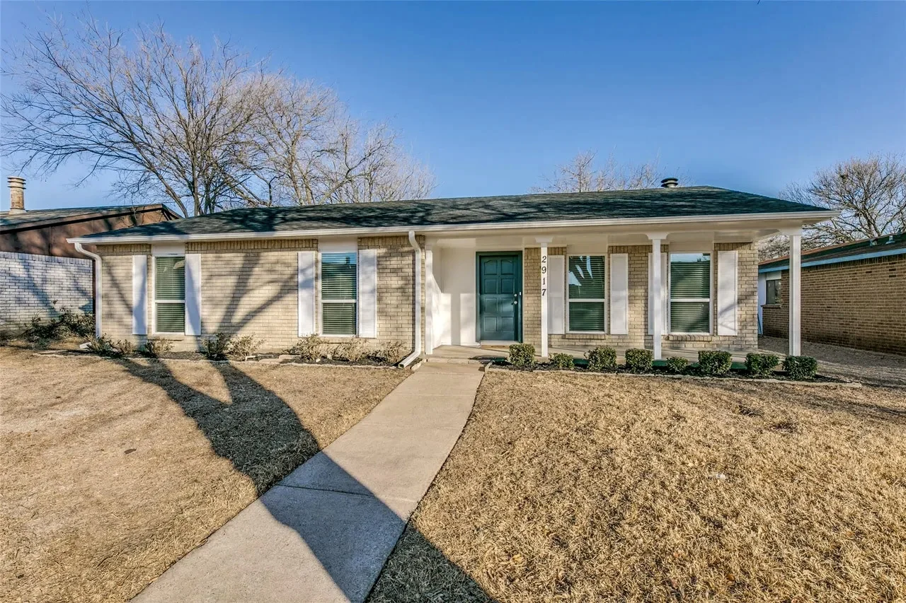 White single-story Dallas ranch with replacement windows, green front door, attached garage, and winter lawn in Dallas, Texas.