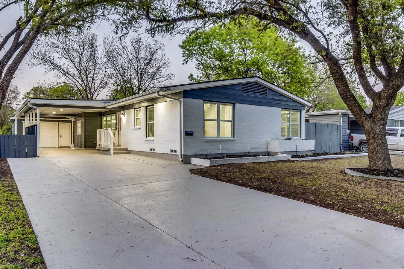 Fresh concrete driveway beside a white brick Dallas home with blue-gray exterior accents and mature trees in Dallas, Texas.