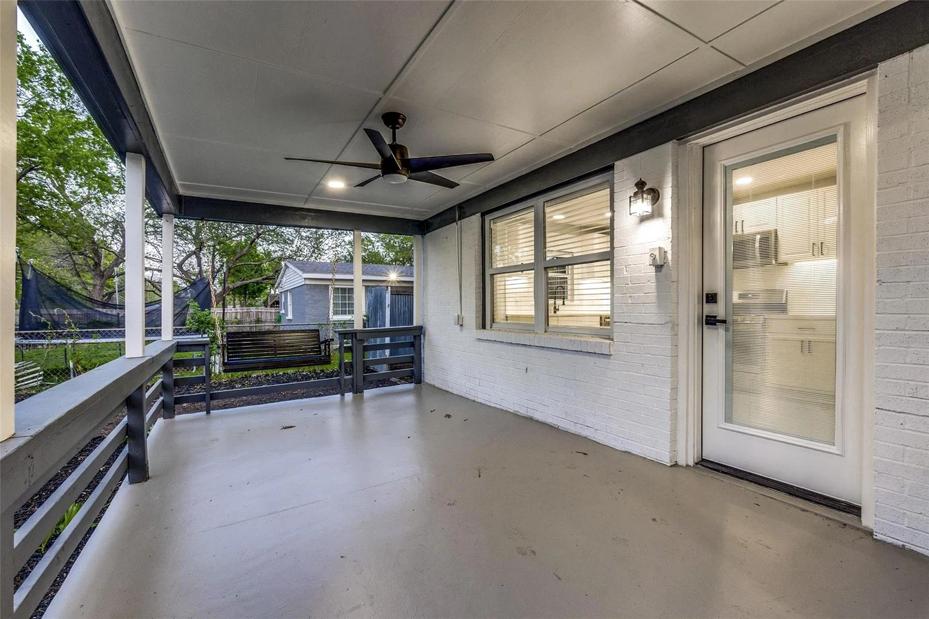Covered backyard patio with gray railings, ceiling fan, painted floor, and direct access to the remodeled interior in Dallas, Texas.
