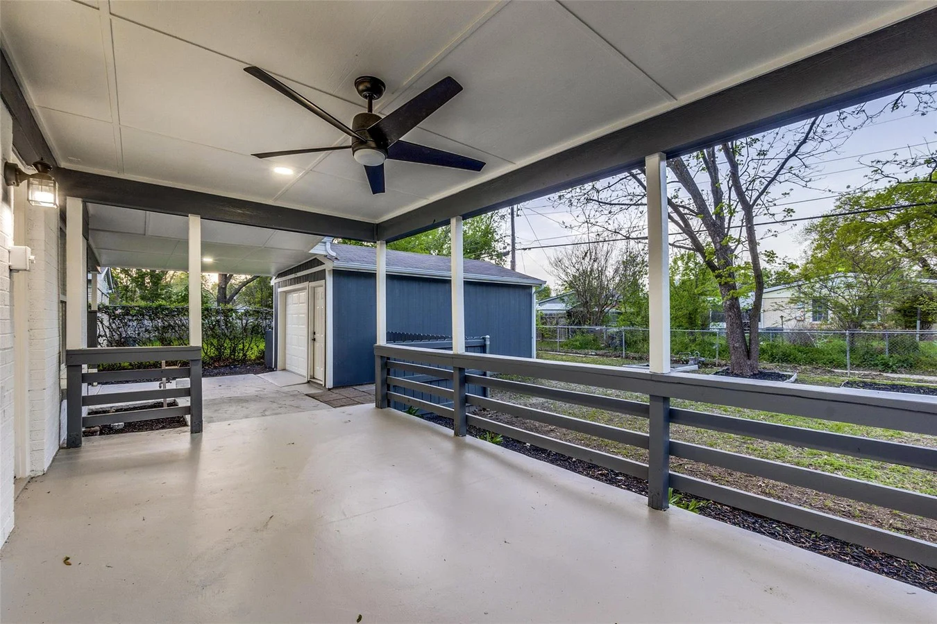 Covered patio with dark railings, blue-gray exterior siding, a ceiling fan, and a view across the backyard in Dallas, Texas.