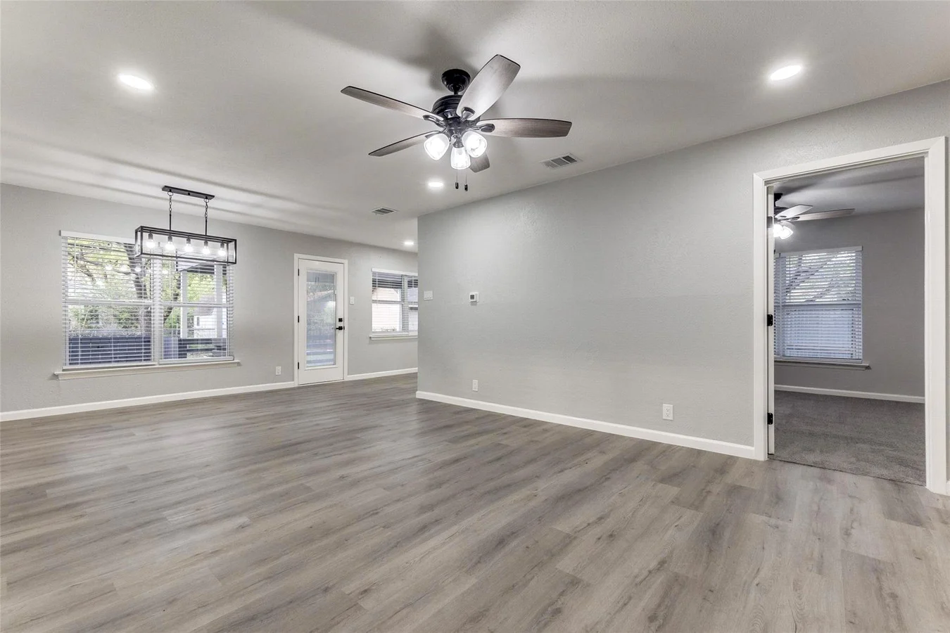 Open living and dining area with gray wood-look flooring, ceiling fan, recessed lighting, and adjacent bedroom access in Dallas, Texas.