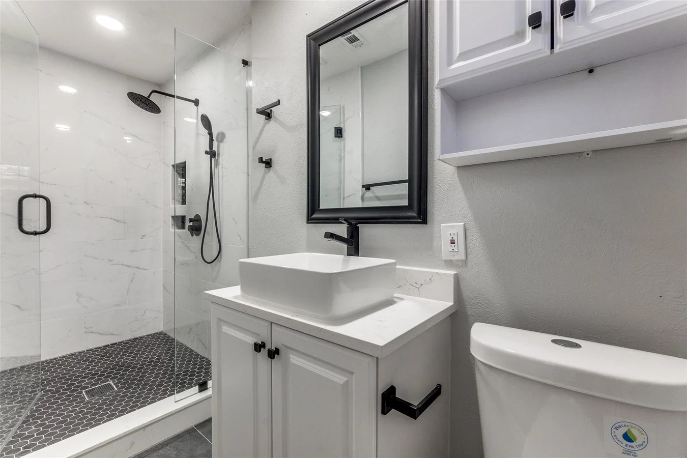 Primary bathroom with a glass shower, marble-look wall tile, white vessel sink, gray vanity, and black fixtures in Dallas, Texas.