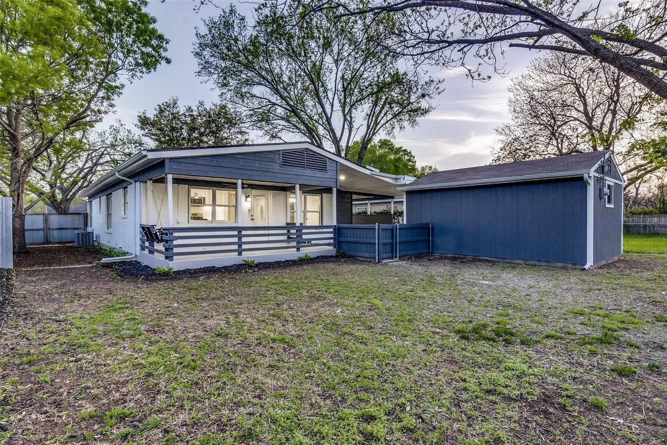 Rear exterior with blue-gray siding, white brick, replacement windows, covered patio, and detached garage in Dallas, Texas.