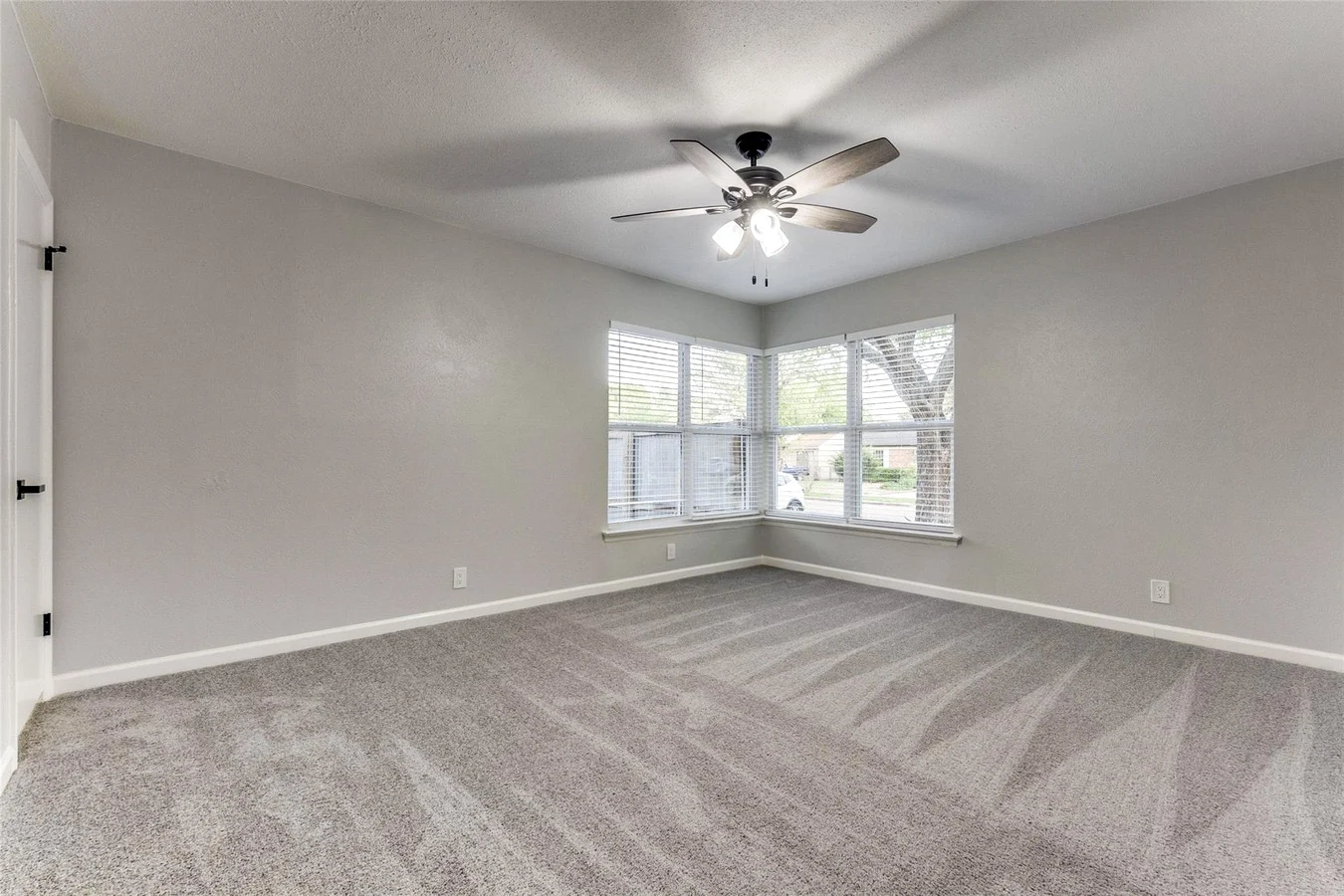 Corner secondary bedroom with new gray carpet, light gray walls, two windows, and a ceiling fan in Dallas, Texas.