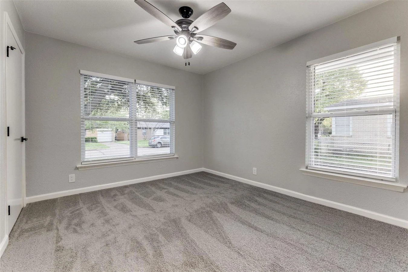Secondary bedroom with new gray carpet, light gray walls, two windows, white trim, and a ceiling fan in Dallas, Texas.