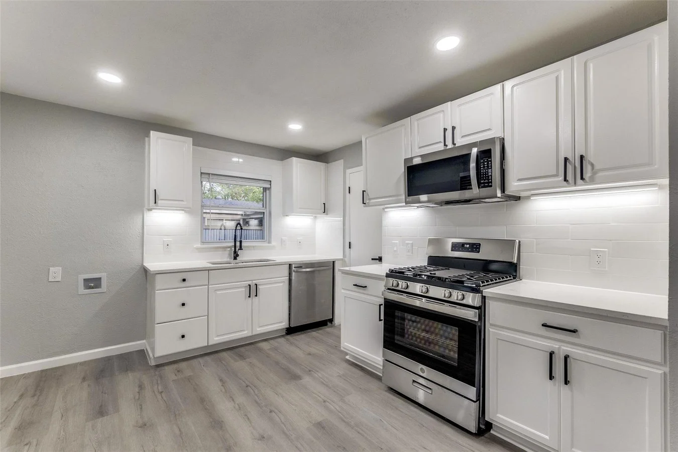 White kitchen with shaker cabinetry, stainless steel gas range, under-cabinet lighting, and gray wood-look flooring in Dallas, Texas.