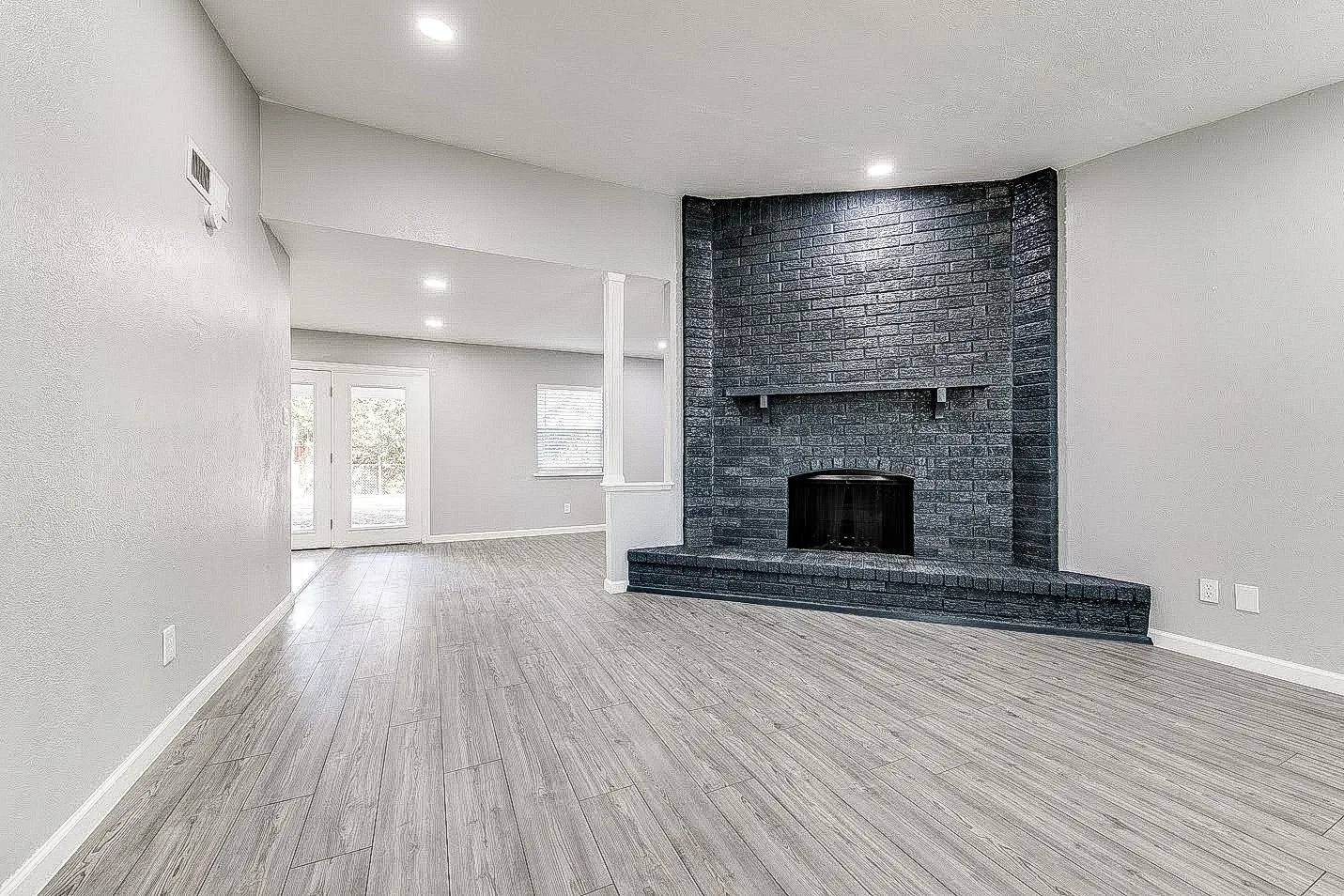 Dallas living room with new wood-look flooring, gray walls, recessed lighting, and black brick fireplace.