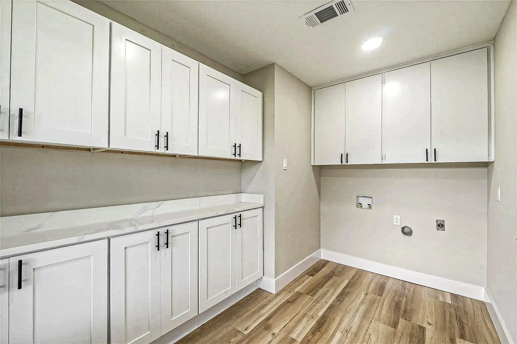 Laundry and utility room with white cabinetry, recessed washer connections, and wood-look flooring in Fort Worth.
