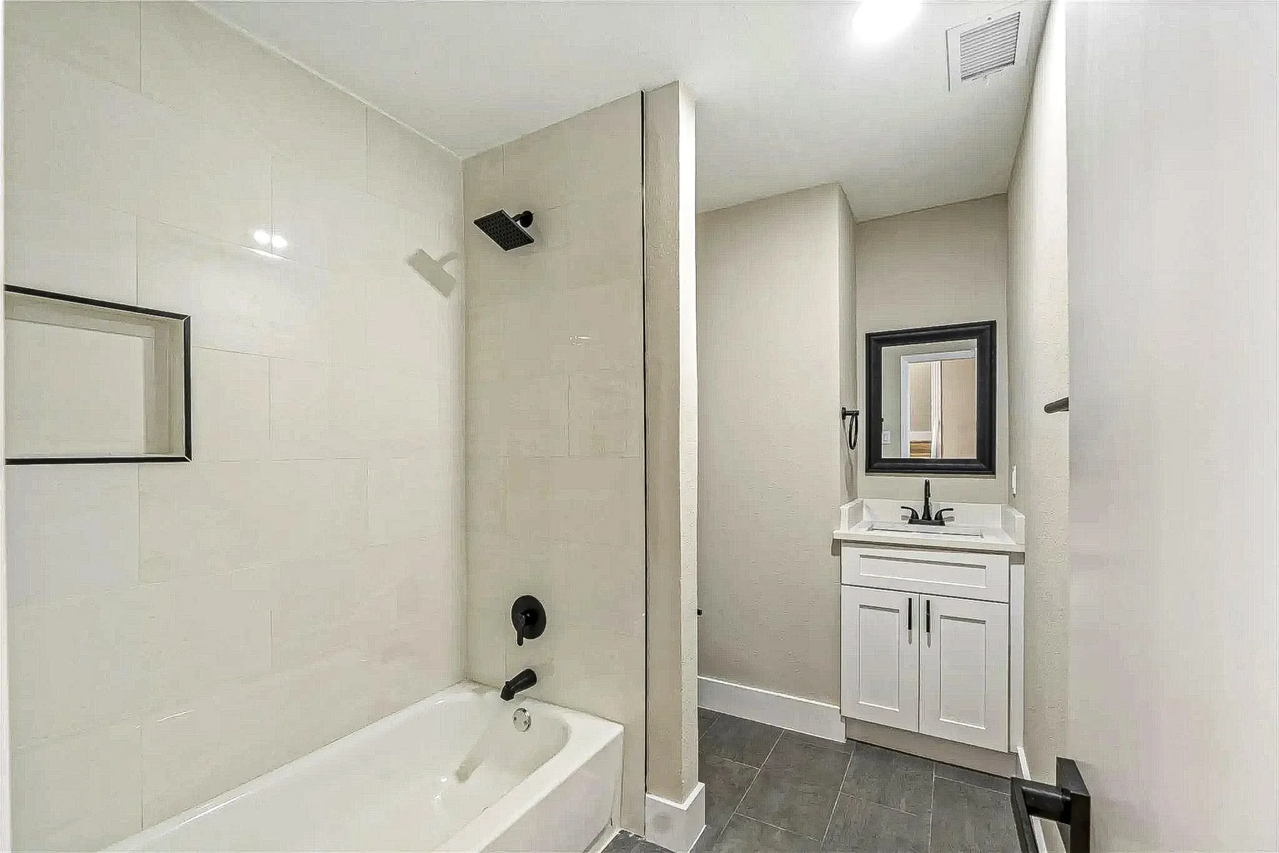 Full bathroom addition with white tub, black shower fixture, marble-look surround, and white vanity in Fort Worth.