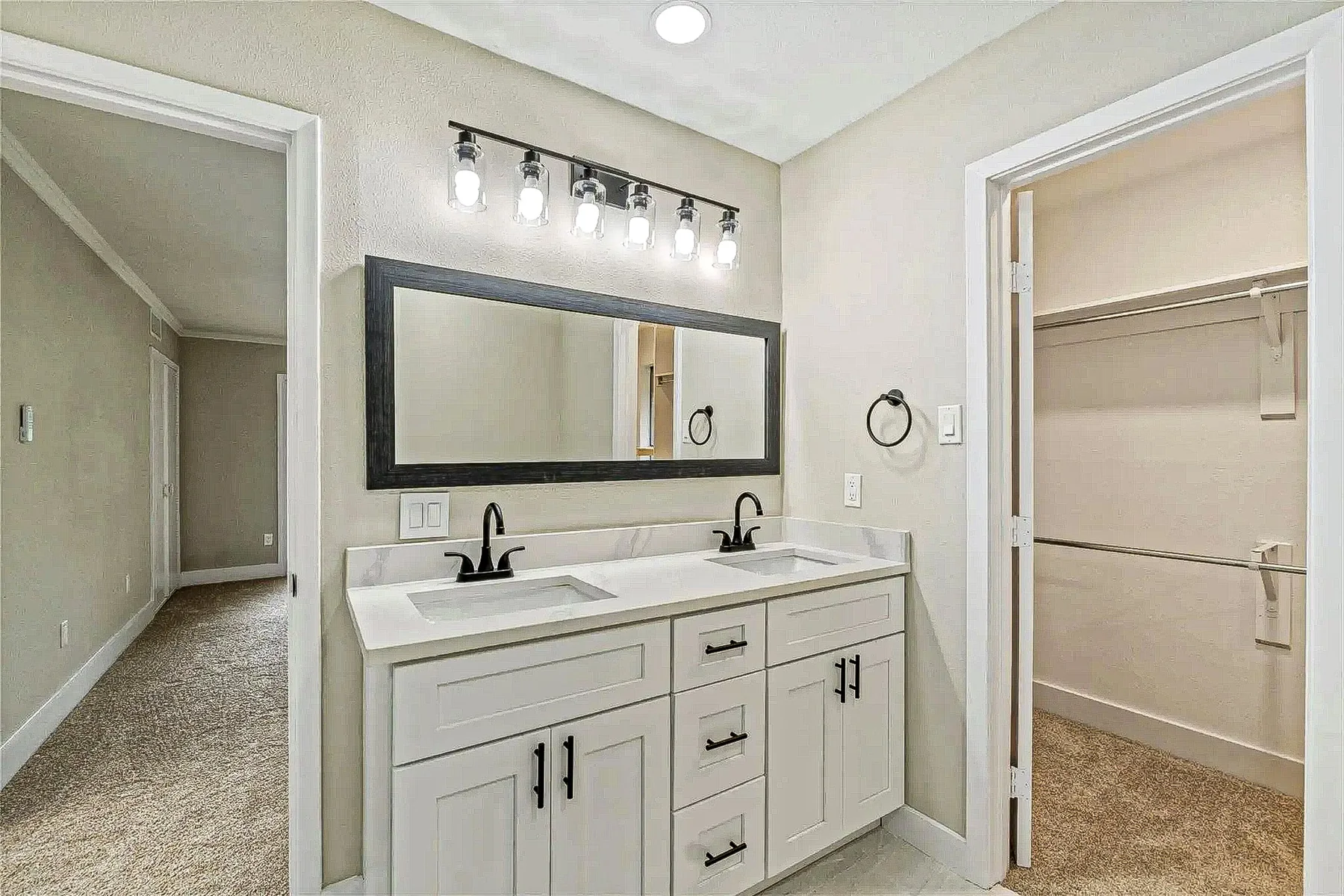 Primary bath vanity with white shaker cabinets, double sinks, black fixtures, and large framed mirror in Fort Worth.