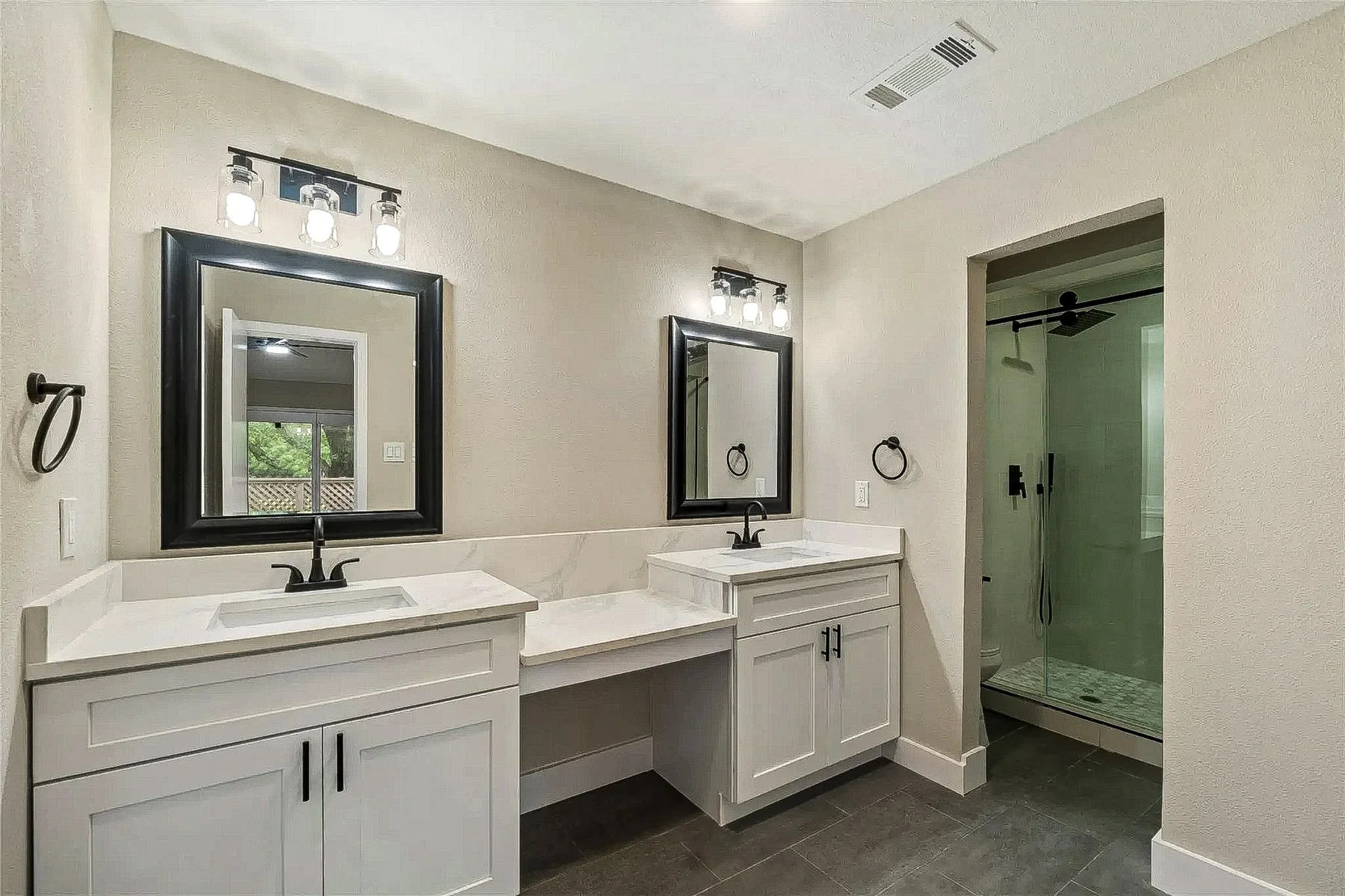 Primary suite bathroom with separate white vanities, makeup counter, black mirrors, and glass shower in Fort Worth.