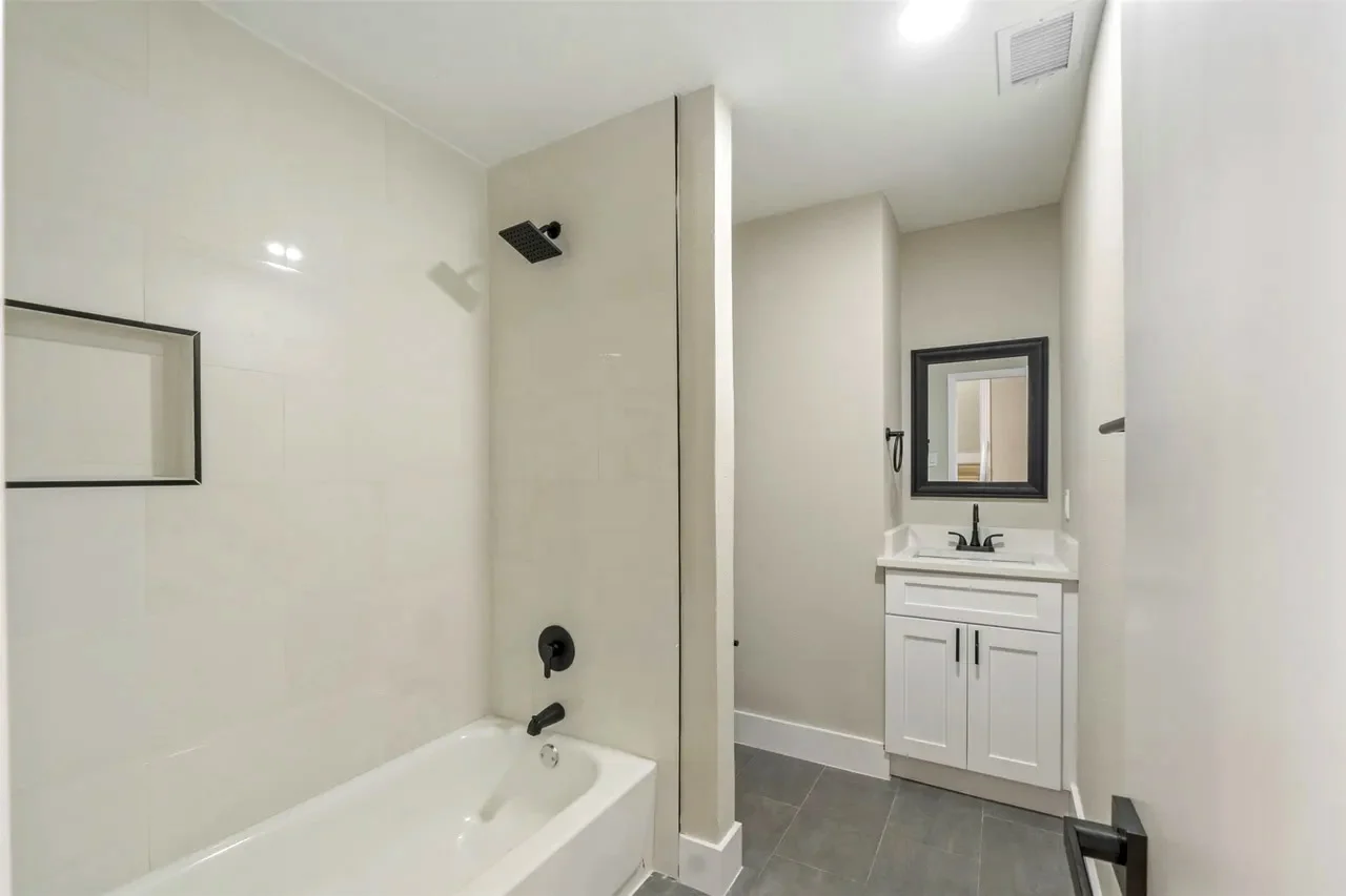 Converted full bathroom with a tub and shower, white vanity, black fixtures, recessed lighting, and neutral tile in Fort Worth, Texas.