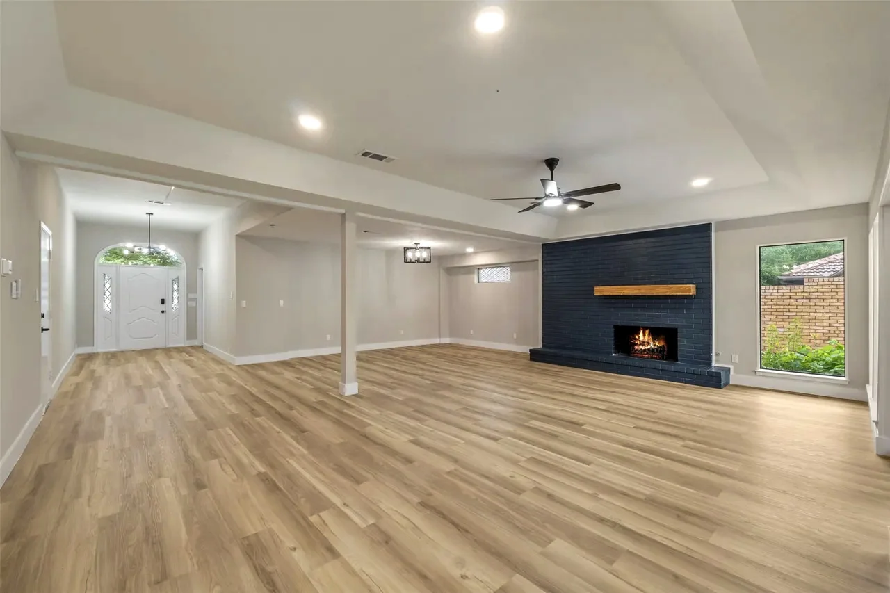 Wide open living room with a black fireplace, wood-look flooring, recessed lighting, and direct sightlines to the entry in Fort Worth, Texas.
