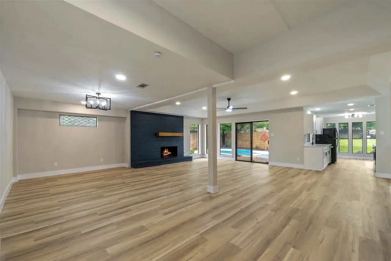 Open whole-home view connecting the living room, black fireplace, white kitchen, dining area, and backyard pool in Fort Worth, Texas.