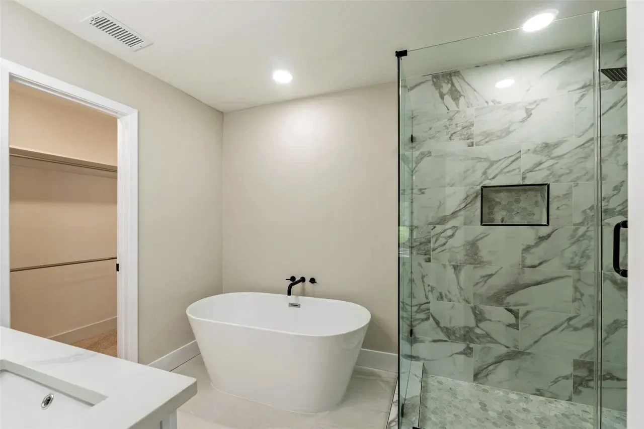 Primary bathroom wet room with a freestanding tub, marble-look shower, frameless glass, and black fixtures in Fort Worth, Texas.